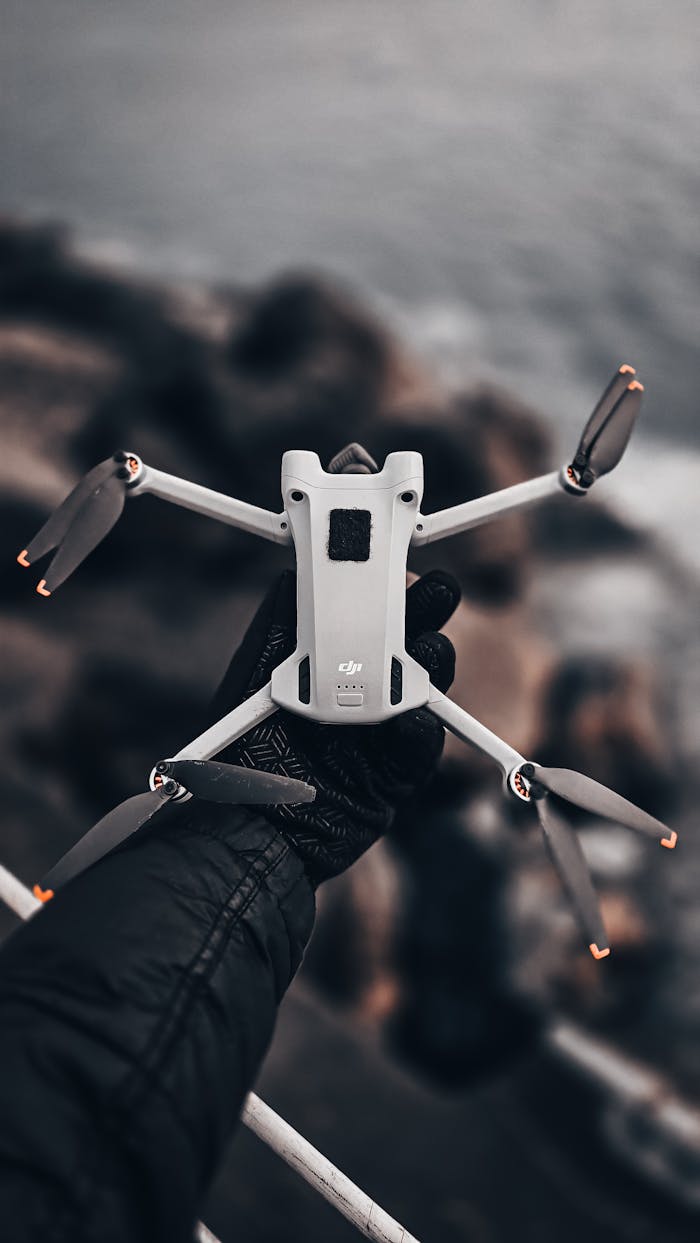 Mastering the First Impression: Your intriguing post title goes here A gloved hand holds a quadcopter drone over a rugged sea cliff edge, ready for aerial shots.